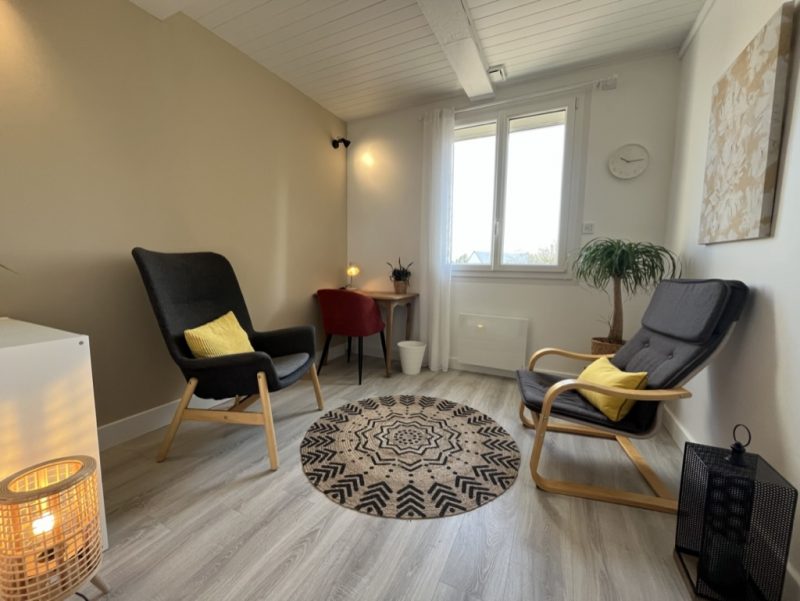 Espace détente avec chaises confortables, une table, un tapis rond et des éléments décoratifs apaisants.