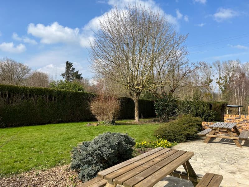 Espace extérieur verdoyant de l'Espace Tulsi, avec des bancs en bois, des arbustes et un ciel bleu.